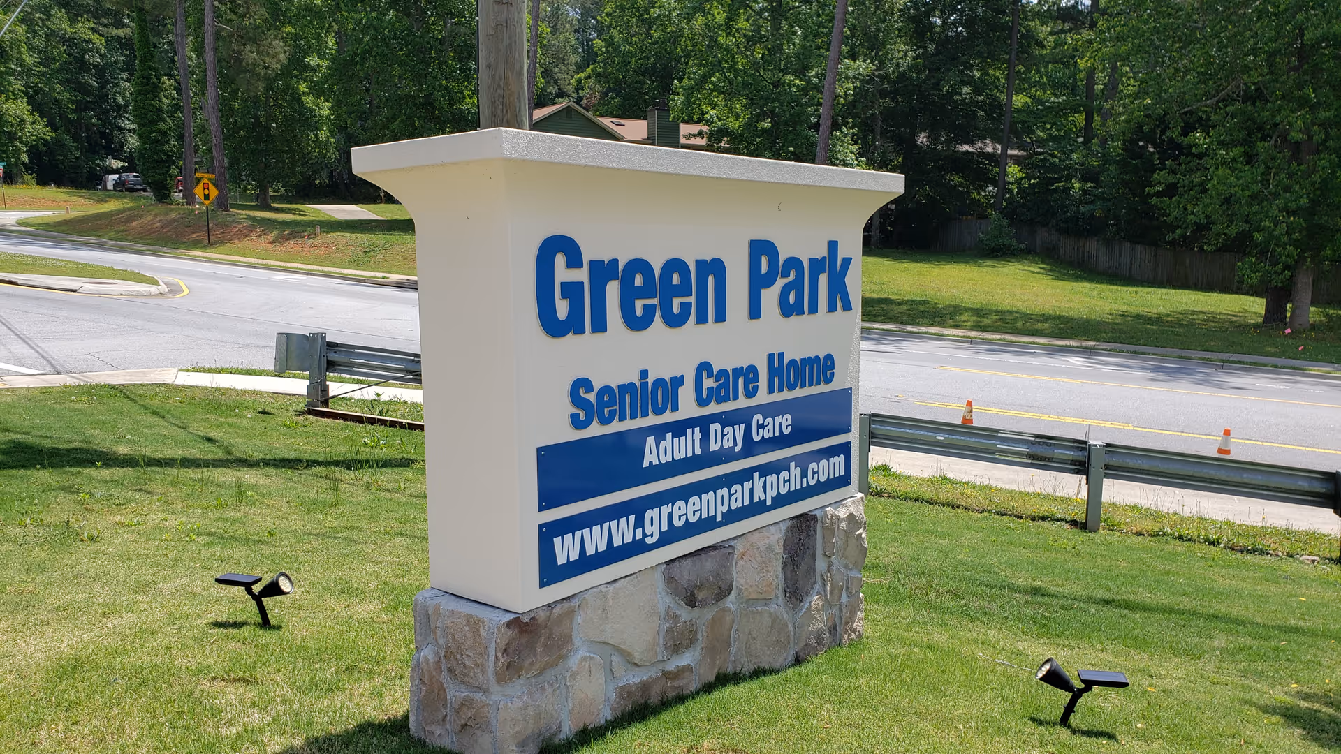 Outdoor sign for Green Park Senior Care Home and Adult Day Care, located on a grassy area near a road with trees and a sidewalk in the background.