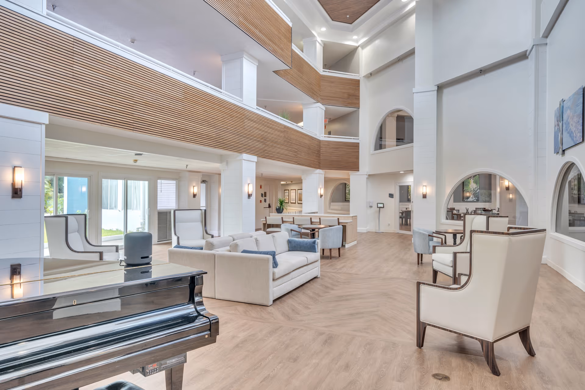 Spacious modern senior living lobby with seating areas, high ceilings, balcony walkways and a grand piano.
