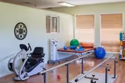 A small exercise room with rehab equipment, benches, exercise balls, and windows.