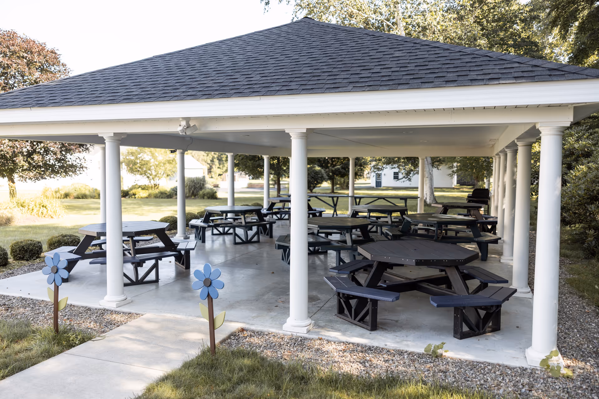 An outdoor pavilion featuring multiple picnic tables and decorative flower sculptures, surrounded by greenery.