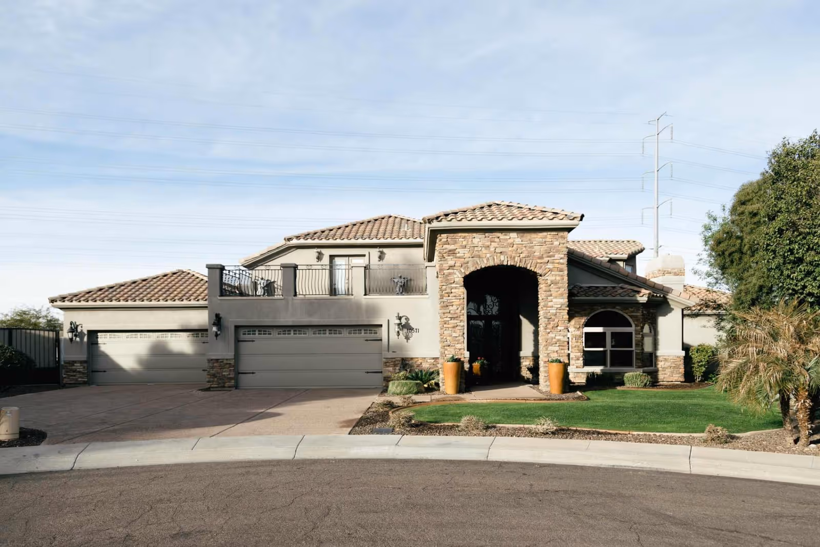 Front exterior of a two-story stucco and stone building with a tiled roof, three-car garage, arched entryway and landscaped lawn.