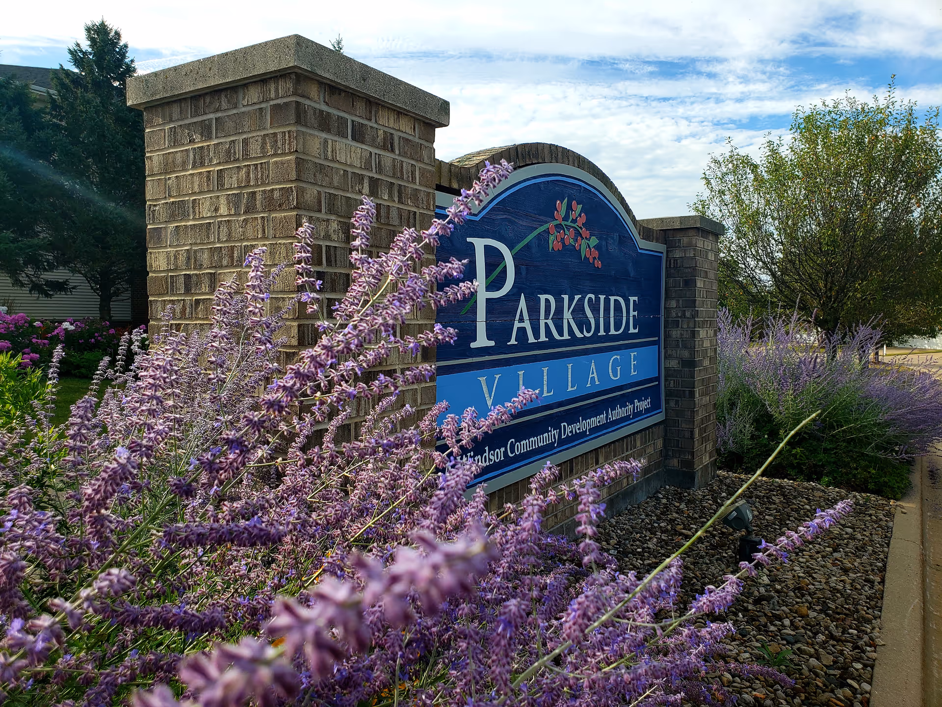 Brick entrance sign reading "Parkside Village" surrounded by purple flowers and landscaping.