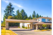 Exterior view of a senior living facility named The Bridge at Mount Vernon, showing a two-story building with a covered entrance driveway, surrounded by trees and a clear blue sky.