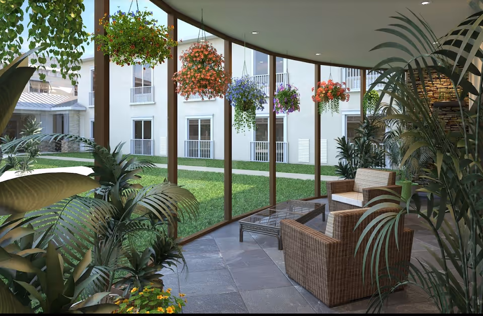 Sunlit indoor seating area with wicker chairs and hanging flower baskets overlooking a grassy courtyard through tall glass windows.