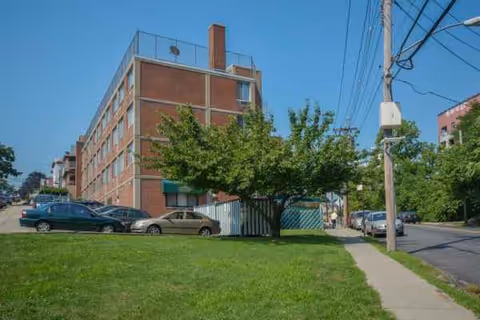 Brick nursing facility on a street with trees, parked cars, and a sidewalk.