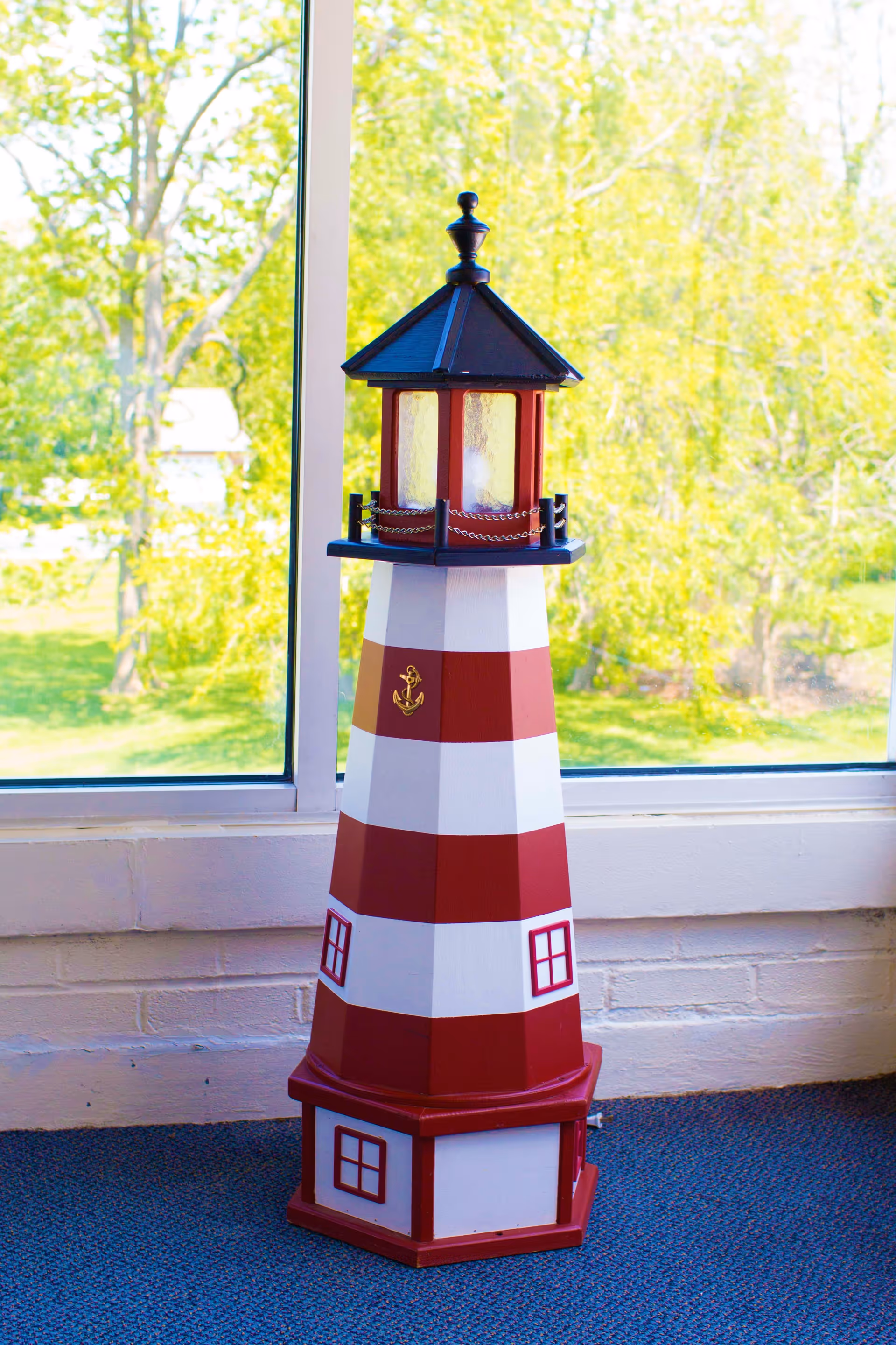 Red-and-white striped decorative lighthouse model standing on a windowsill with green trees visible outside.
