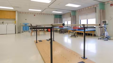 Bright therapy room with parallel bars and exercise equipment in a senior living facility.