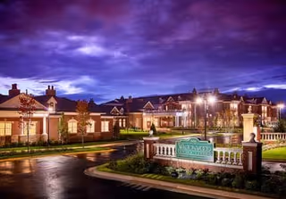 Exterior view of Waltonwood at Ashburn senior living facility at dusk, showing well-lit buildings, landscaped grounds, and a prominent entrance sign with a dramatic purple and blue sky in the background.