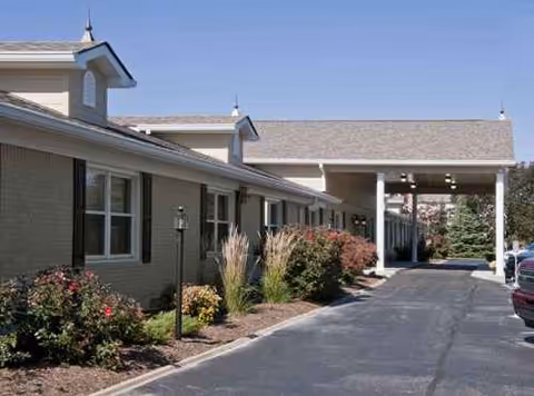 Exterior view of a beige senior care facility with a landscaped driveway.