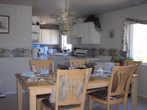 A dining room with a wooden table, chairs, and place settings in a bright kitchen area.