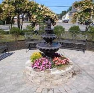 Three-tier fountain encircled by a flower-filled stone planter in an outdoor courtyard.