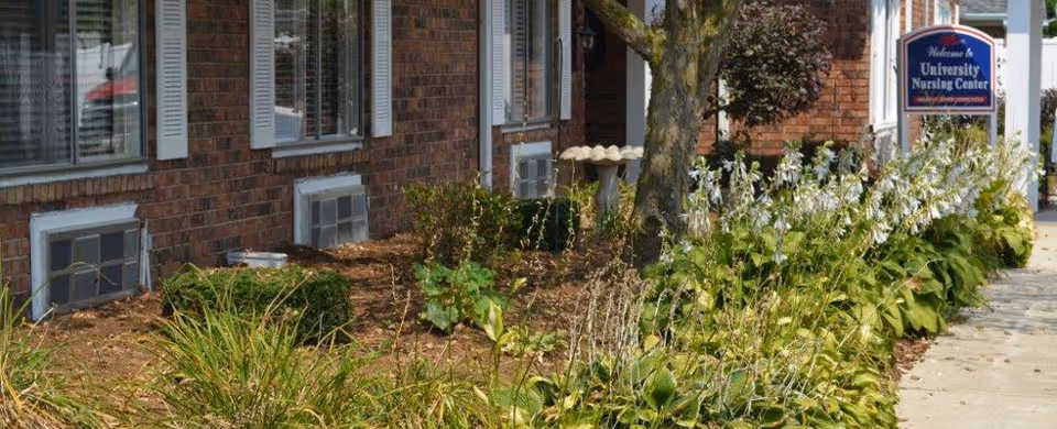Brick exterior of the University Nursing Center showing a landscaped bed, sidewalk, and a welcome sign.