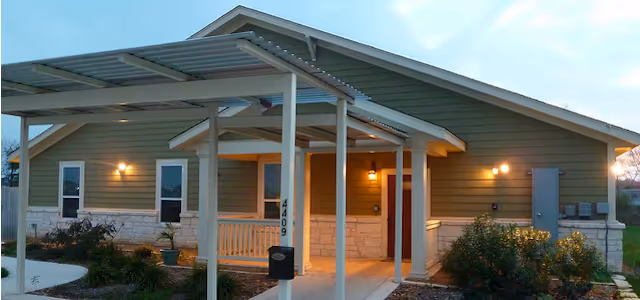 Front entrance of a single-story building with a covered walkway, porch, and exterior lights at dusk.