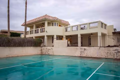Two-story cream facility with balconies, a gated outdoor area, and a turquoise court.