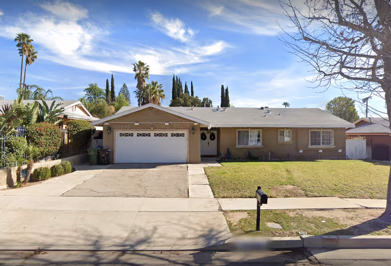 Single-story beige house with an attached two-car garage, front lawn, driveway and mailbox under a blue sky.