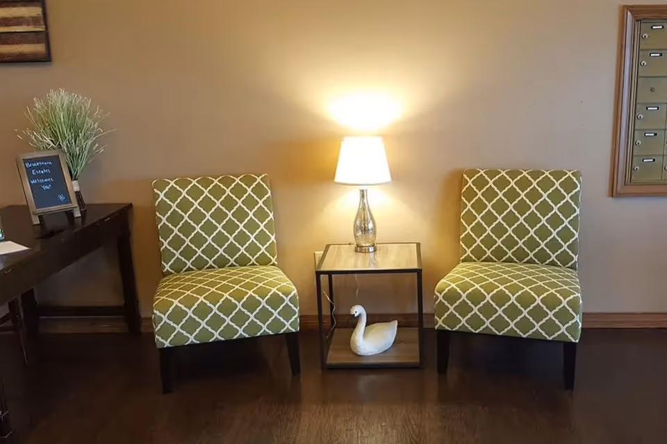 Two green patterned chairs flank a small side table with a lamp and a decorative swan in a seating area.
