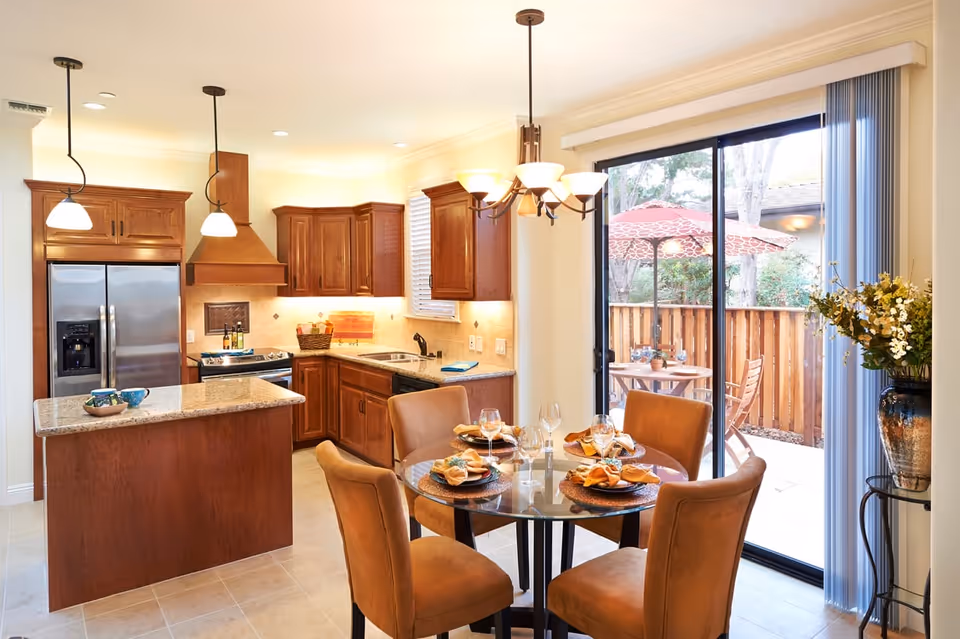 Bright kitchen and dining area with wooden cabinets, a central island, and a round table set for four beside sliding glass doors to a patio.