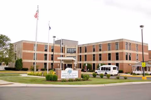 Brick senior living facility exterior with entrance, flags, and a white van.