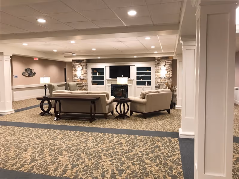 Comfortable common lounge with sofas and armchairs facing a built-in TV and fireplace flanked by stone columns.