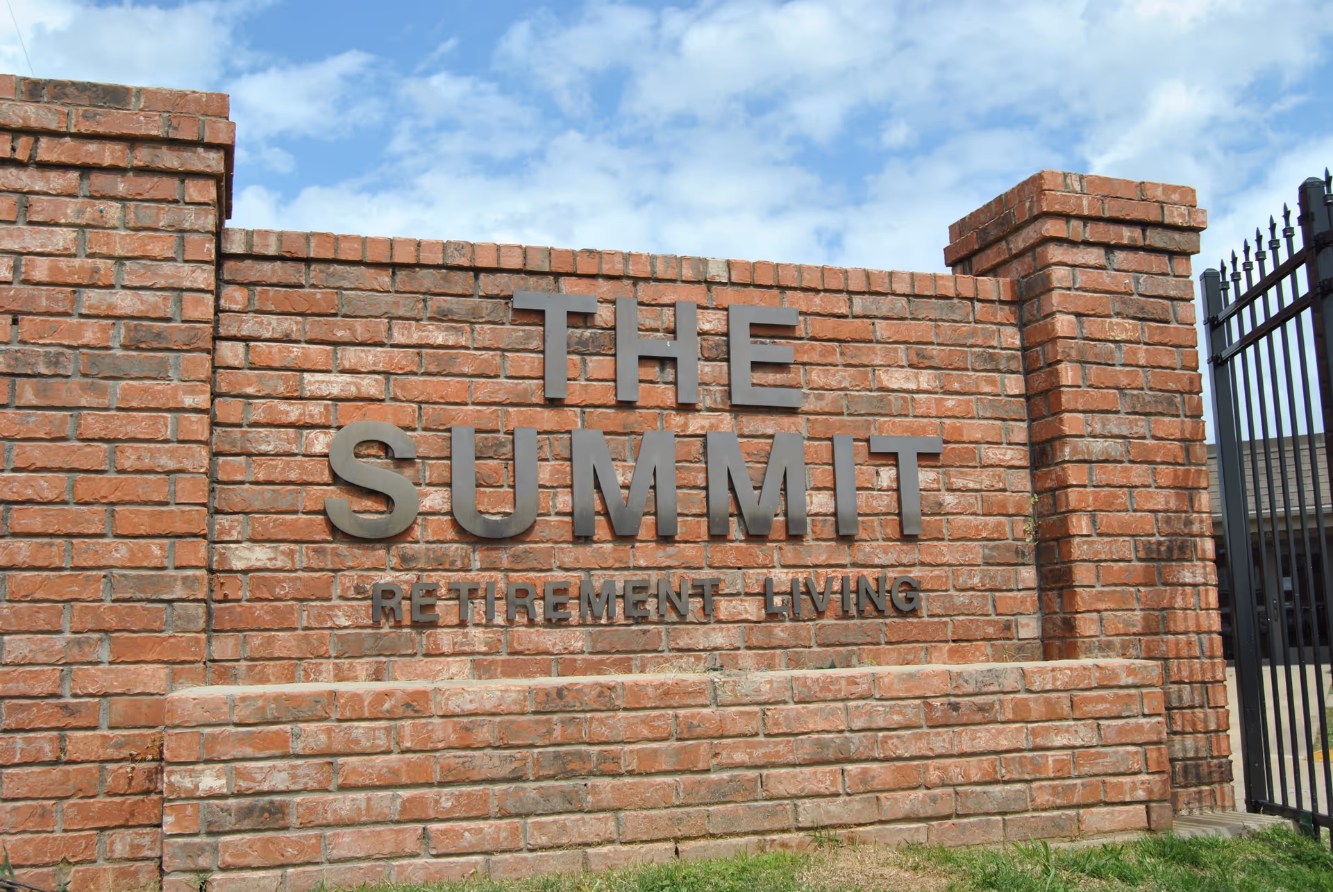 Brick entrance sign reading 'THE SUMMIT' with 'RETIREMENT LIVING' below beside a black gate.
