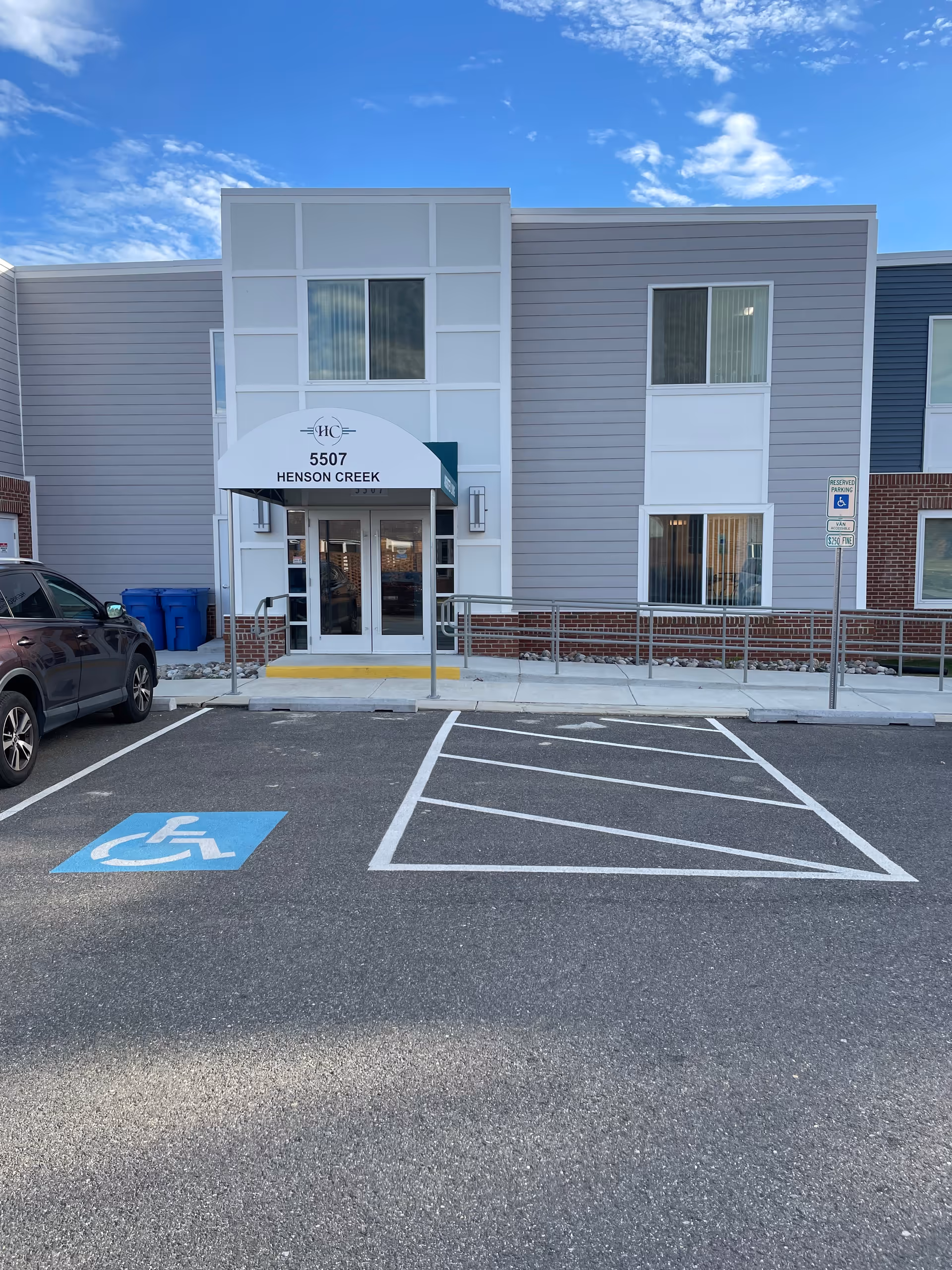 Front entrance of Henson Creek Assisted Living Facility with an awning reading "5507 HENSON CREEK", accessible parking spaces and a sidewalk ramp.