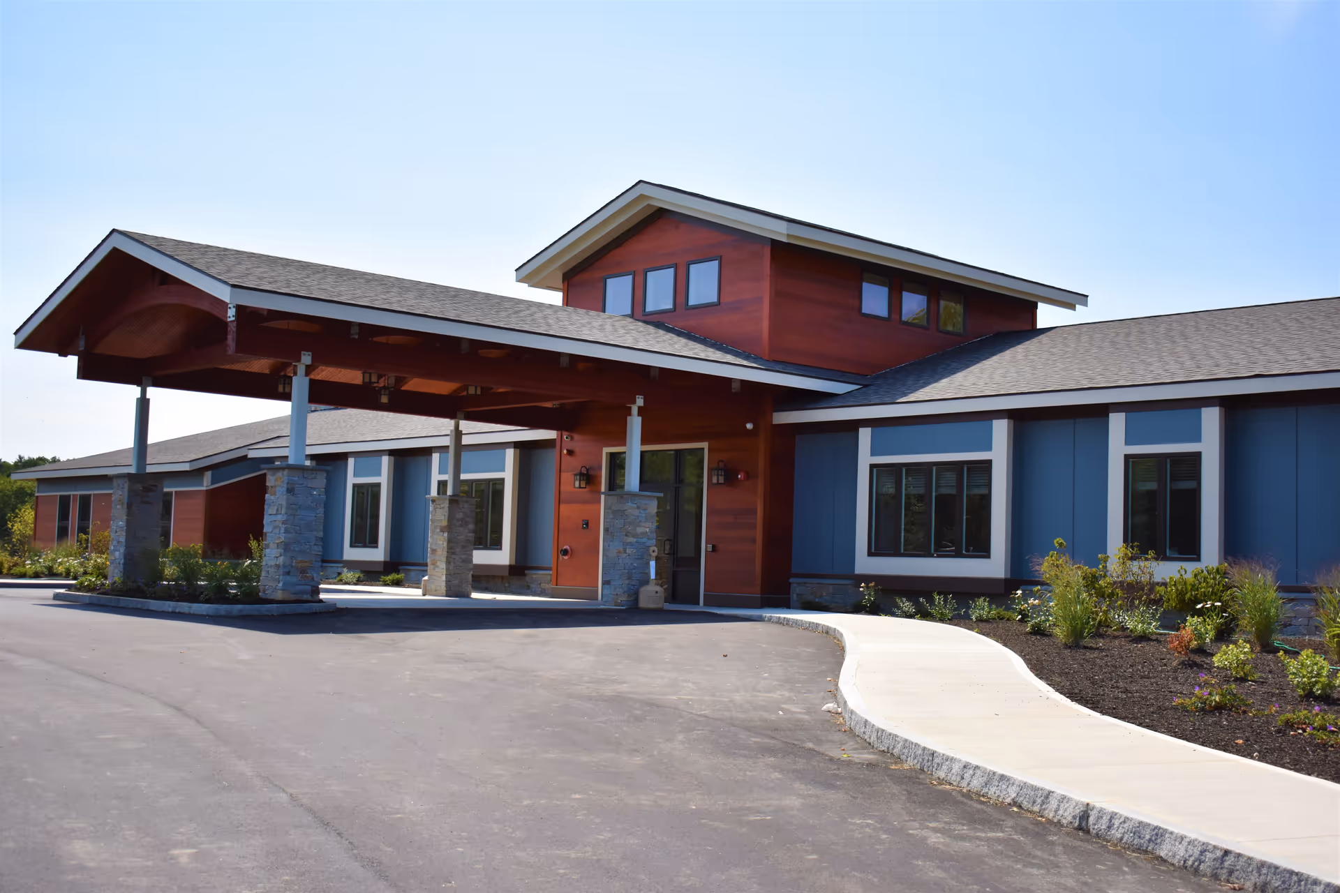 Front exterior of a modern senior living facility with a covered entrance porte-cochere and landscaped driveway.