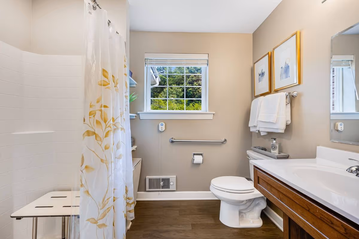Bright accessible bathroom with a shower and curtain, toilet, sink vanity, grab bar, and a window.