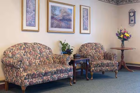 Two floral upholstered chairs flank a small table with a vase of flowers in a lounge.