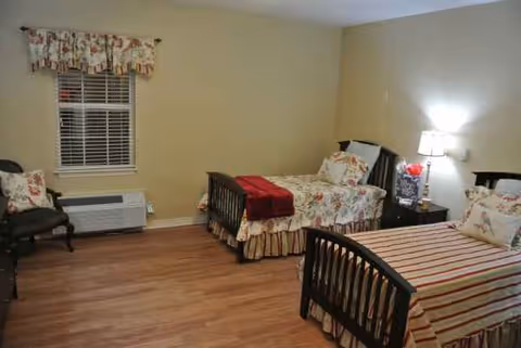 A shared bedroom with two single beds, floral quilts, window, and nightstand lamp.