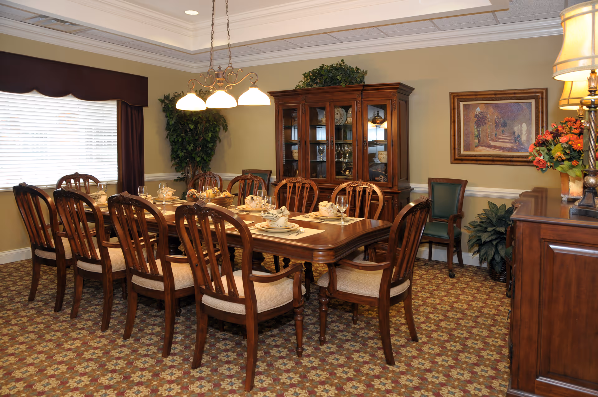 Formal dining room with a long wooden table set for a meal, matching chairs, a chandelier, and a china cabinet.