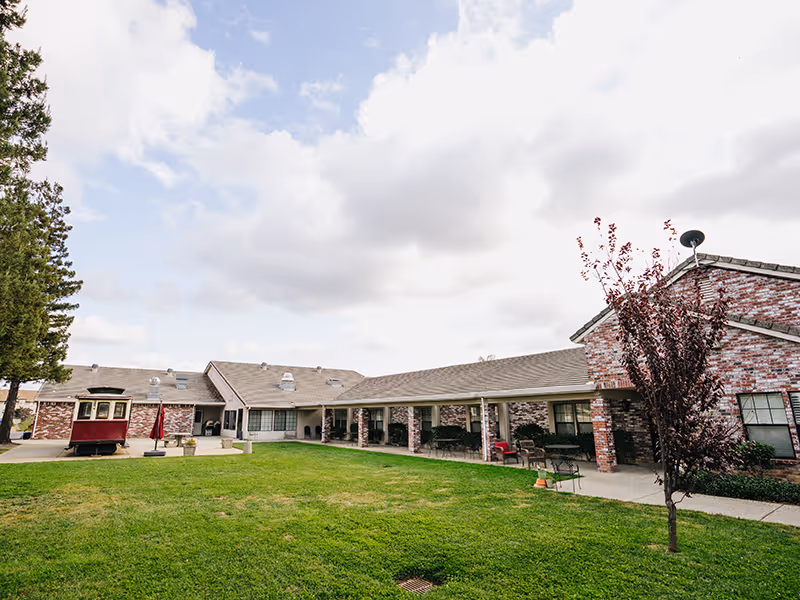 Brick single-story assisted living building with a covered walkway surrounding a grassy courtyard under a cloudy sky.