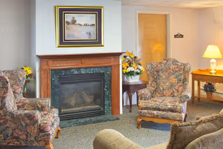 Cozy sitting area with a fireplace, floral upholstered armchairs, a framed painting, side tables with flowers and a lamp.