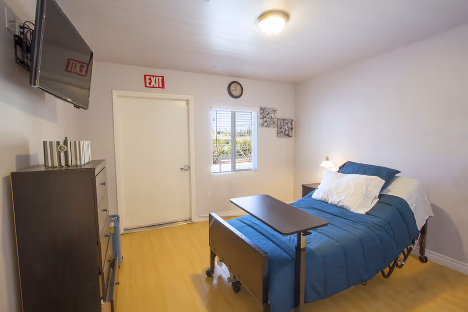Single bed with blue bedding, dresser, TV, and exit sign in a small bedroom.