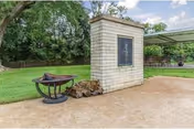 Outdoor area with a fire pit, a stack of firewood, and a stone structure with a mounted plaque, surrounded by green grass and trees in the background.