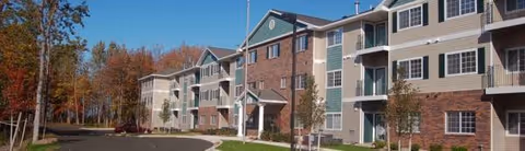 Exterior view of Maxwell Place senior living, a brick-and-siding apartment building with trees.
