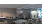 Interior of a chapel with rows of pews facing an altar and stained glass windows along the right wall.