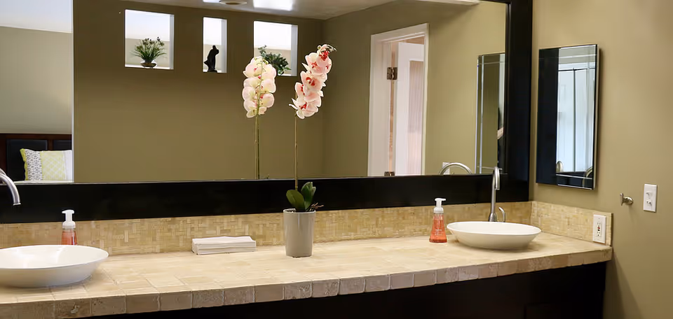 Double-sink bathroom vanity with a large mirror, orchid plant, and soap dispensers on a tiled countertop.