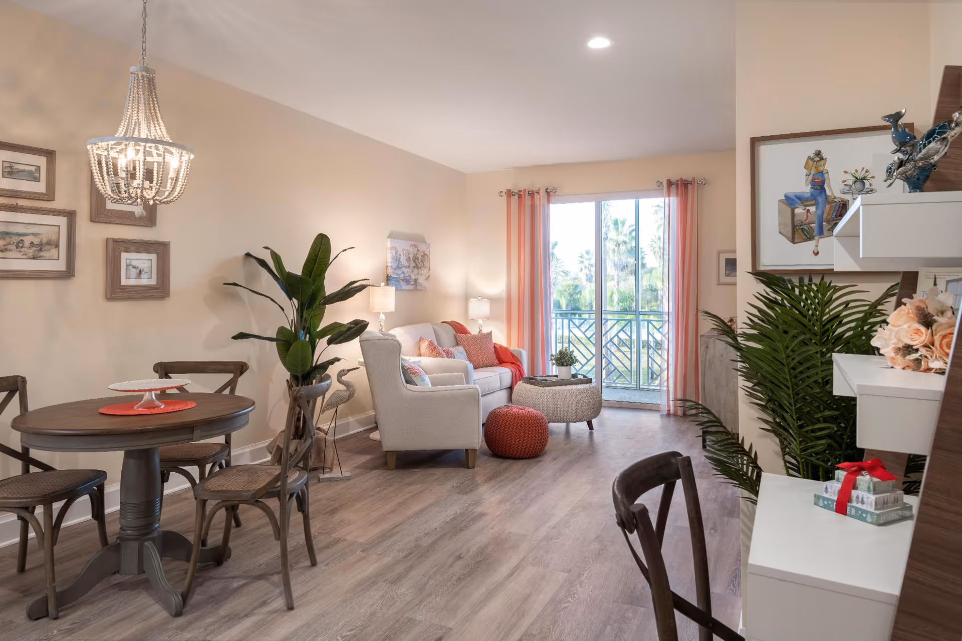Open living room and dining area with a round dining table, armchair and sofa, plants, and a sliding glass door to a balcony.