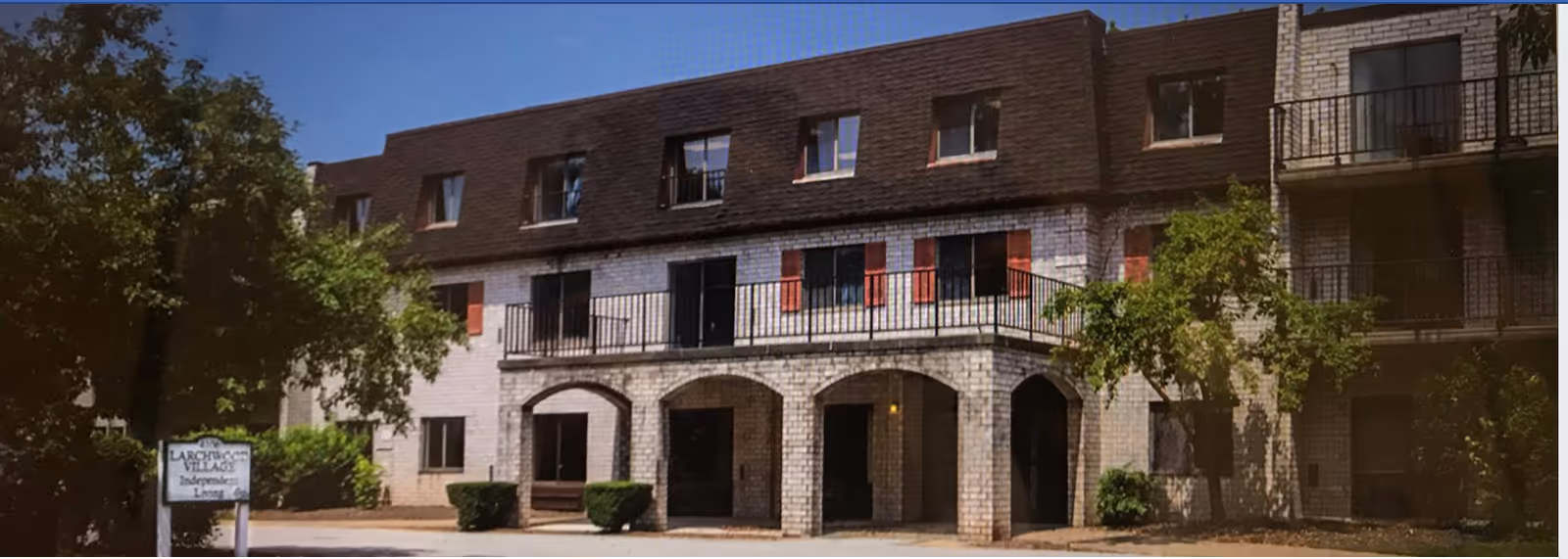 Exterior view of brick senior living facility with arches and balconies.