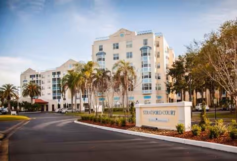 Exterior view of Stratford Court of Palm Harbor, a multi-story senior living facility with palm trees.