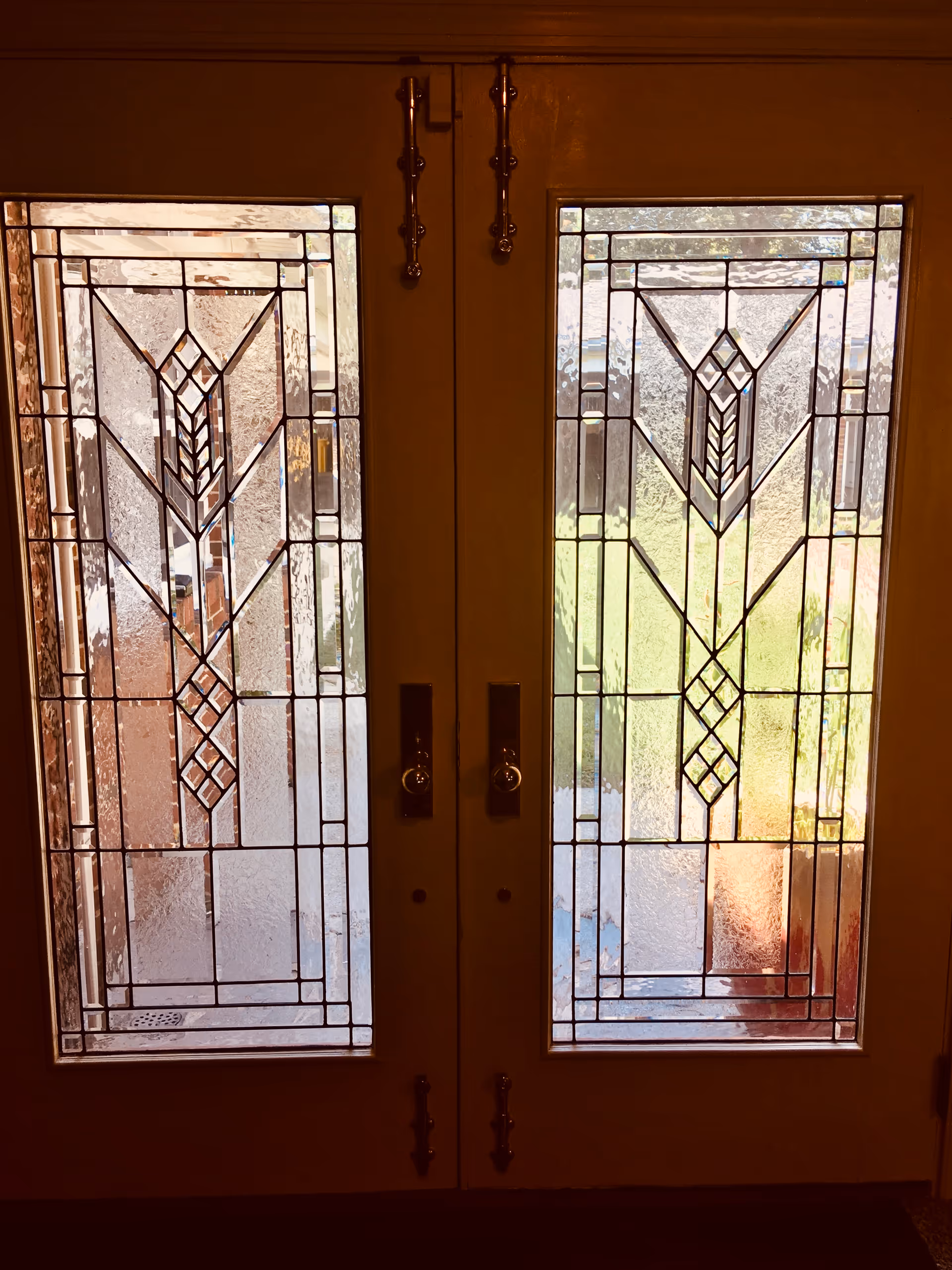 Double doors with decorative stained glass panels featuring geometric and diamond patterns, allowing light to pass through and partially revealing an outdoor area.