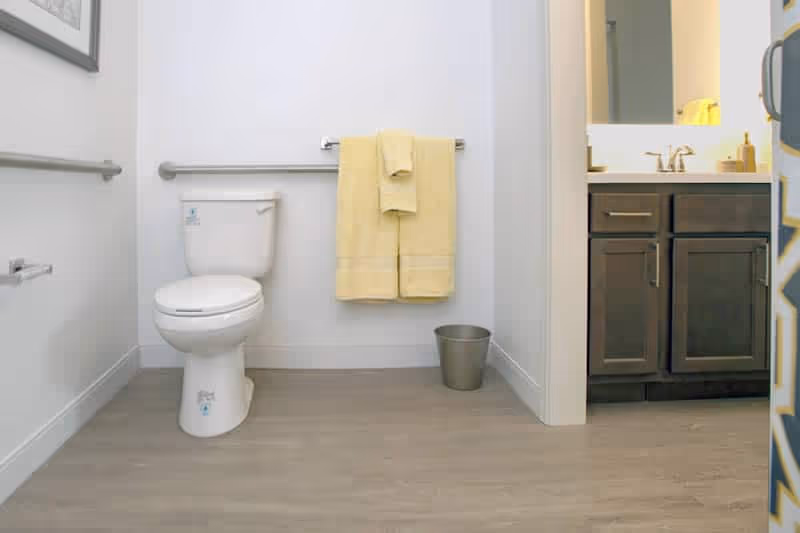 Bright accessible bathroom with a toilet, wall-mounted grab bars, yellow towels, a sink vanity, and a small waste bin.