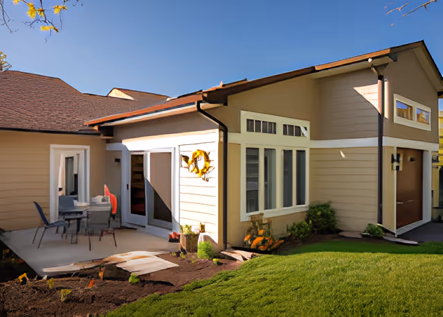Exterior view of a beige single-story building with a small patio, sliding glass door, and manicured lawn.