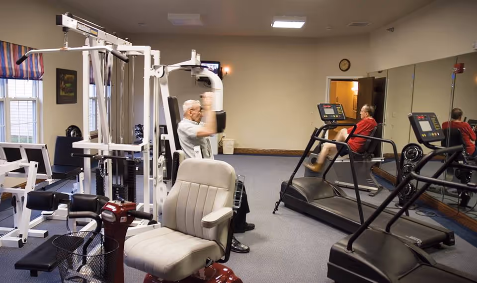 Fitness room with exercise machines, treadmills, mirrors, and two people using the equipment.