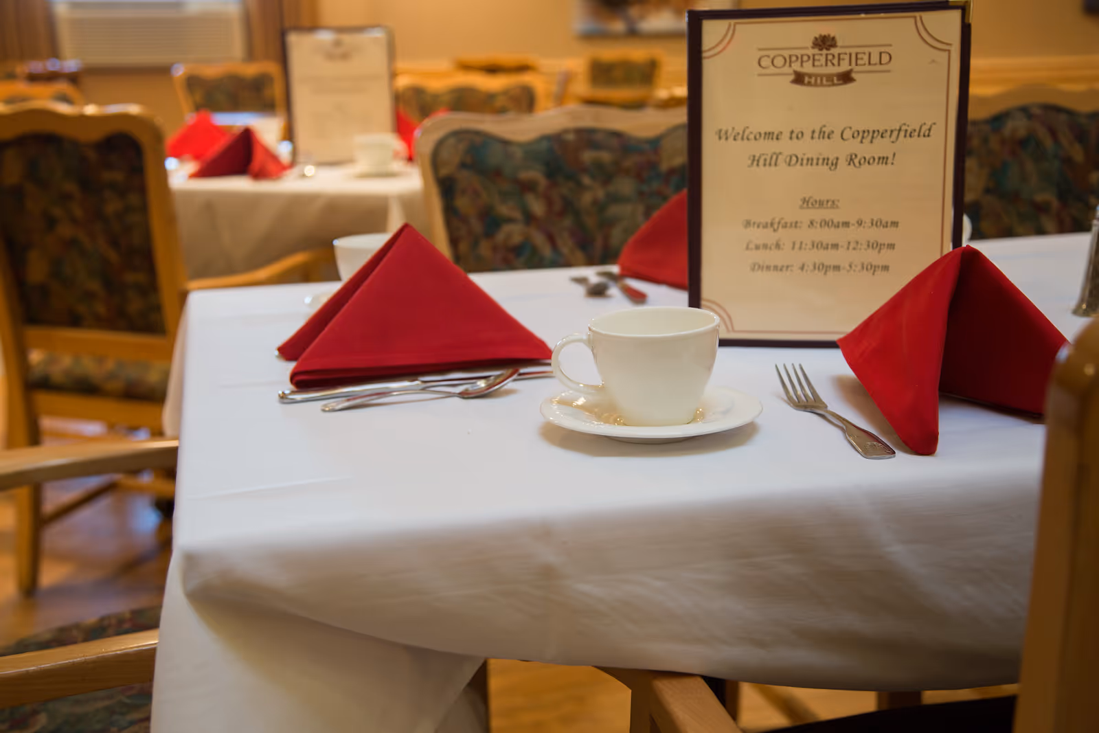 Copperfield Hill dining room table with red napkins, cup, and menu.