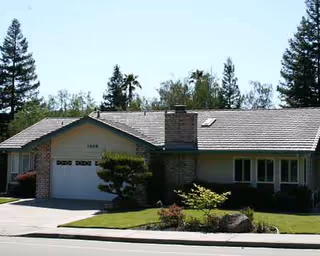 Single-story suburban house with a two-car garage, manicured lawn, and surrounding trees.