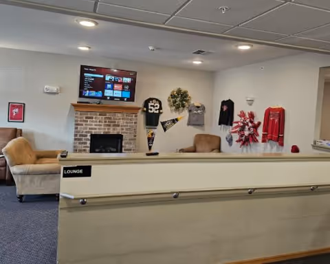 Community lounge with sofas, a brick fireplace, wall-mounted TV, and sports memorabilia on the wall.