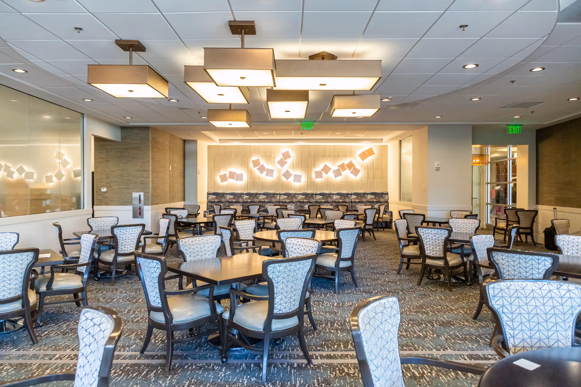 Spacious dining room with multiple round tables and patterned chairs under modern ceiling lights.