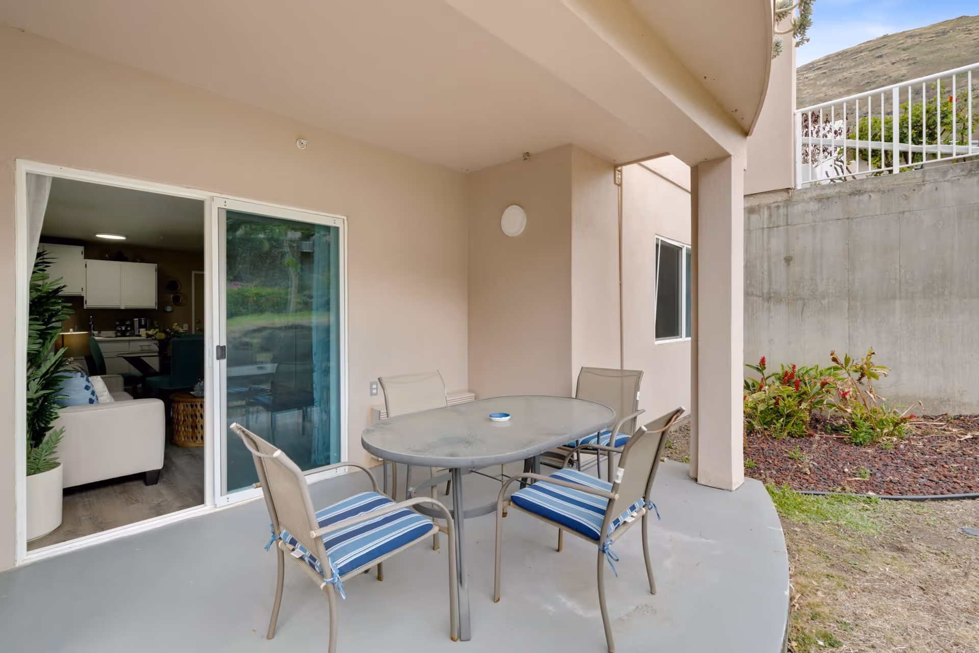 Covered outdoor patio with a round glass table and four chairs beside a sliding glass door into the living room.