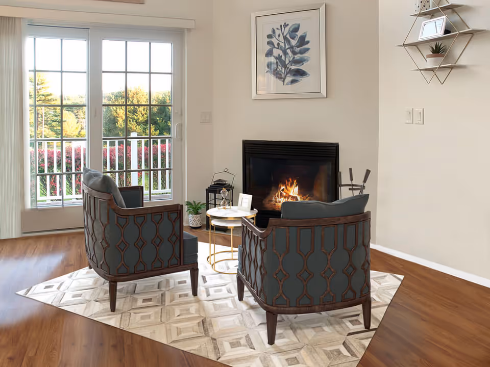Two upholstered armchairs in a living room facing a lit fireplace beside sliding glass doors opening to a balcony.